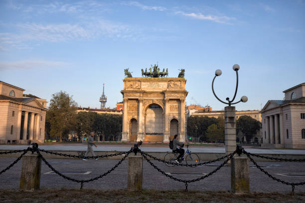 Downtown street view, Milan, Italy in the morning. Pedestrian and cyclist passing by Arch of Peace in the background.