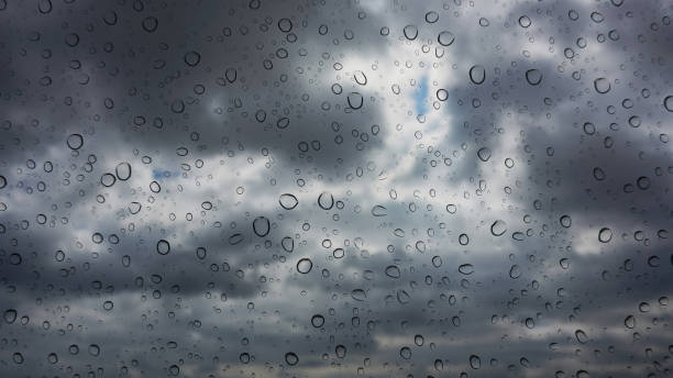 Focus on raindrops on window pane with storm clouds defocused beyond