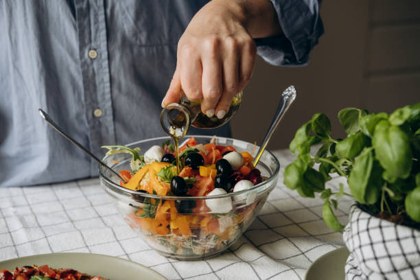 istock Women's hands cooking and mixing salad with tomato  olives mozzarella vegetables arugula dressing with balsamic vinegar and olive oil in a large bowl a healthy balanced meal 2197135937