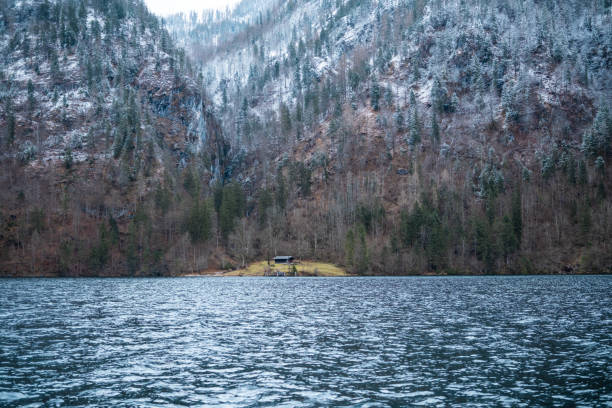 A peaceful cabin rests by a lake with snow-dusted mountains in the background.