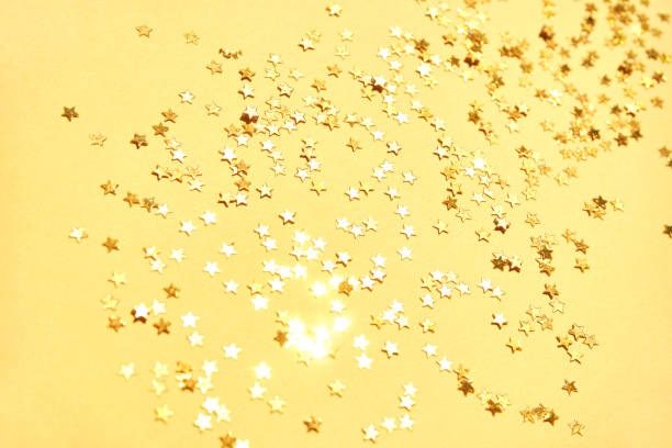 Golden star confetti scattered on yellow background for festive celebration and sparkle themes.