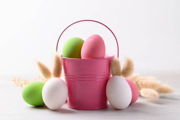 istock White easter eggs with bunny rabbit ears and colorful easter eggs in pink bucket on white background 2197166907