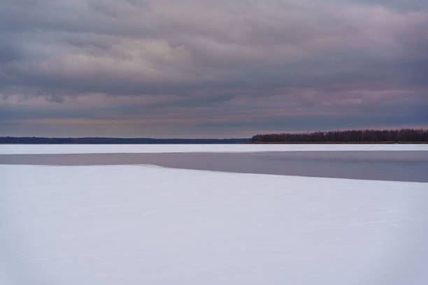Snow-covered frozen lake under a cloudy winter sky. A tranquil and serene landscape capturing the stillness and beauty of nature in the cold season