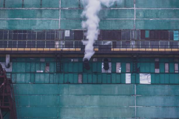 An industrial building under renovation, covered with green scaffolding mesh, emitting steam from a vent, showcasing urban architecture and construction work in progress