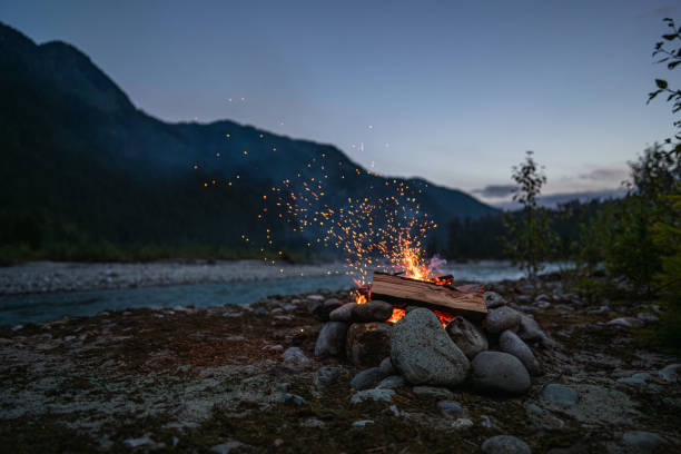 Cozy campfire with glowing sparks located in a peaceful mountain landscape, surrounded by twilight ambiance and natural serenity. Perfect for illustrating camping, adventure, and connection with the outdoors.