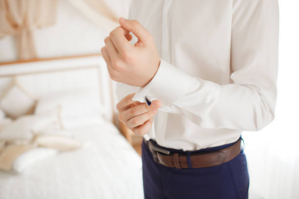 A man buttons up a white shirt in a hotel room. Close-up of a young man buttoning his shirt buttons. Man going to a business meeting