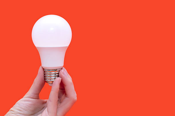 istock Energy saving light bulb in hand on orange background with free space for text 2197174639