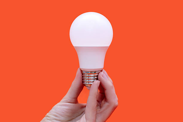 istock Energy saving light bulb in hand on orange background 2197174959