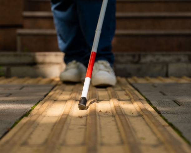 istock A blind woman walks outdoors using a cane along a tactile yellow tile. 2197178318