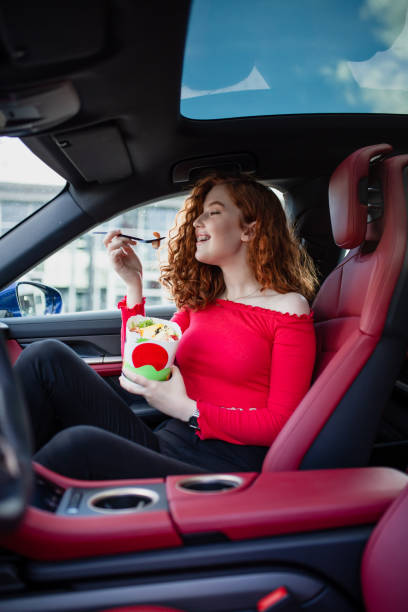 istock Young woman eats healthy meal with chopsticks in car 2197178459