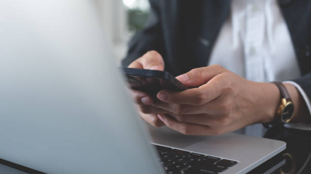 istock Close up, businesswoman using mobile smart phone during working on laptop computer at office. Business woman in business sitting at table using smartphone, surfing the internet 2197182295