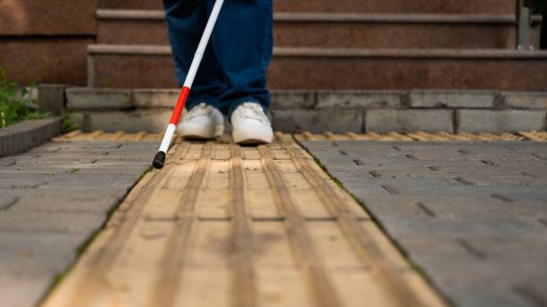 istock A blind woman walks outdoors using a cane along a tactile yellow tile. 2197183085
