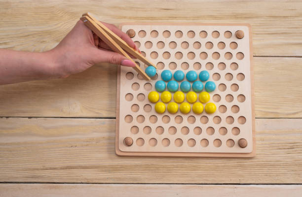istock Educational game, wooden board for sorting according to the Montessori system. In his hands are wooden tweezers with a ball. 2197188780