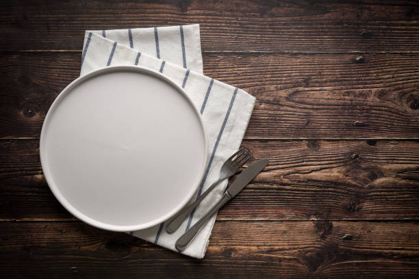 istock Top view of empty ceramic white plate, fork and table knife on wooden table 2197188792