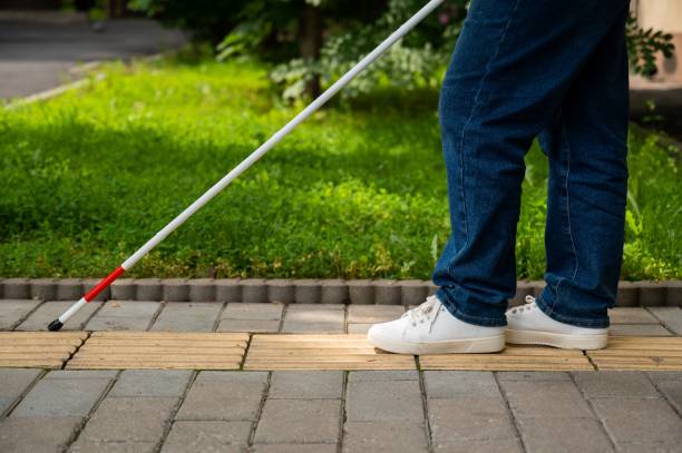 istock A blind woman walks outdoors using a cane along a tactile yellow tile. 2197199368