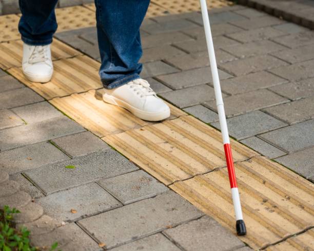 istock A blind woman walks outdoors using a cane along a tactile yellow tile. 2197199657