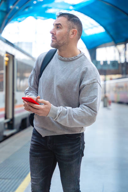 istock Focused Man Holding Red Smartphone at Train Station.vertical 2197201743