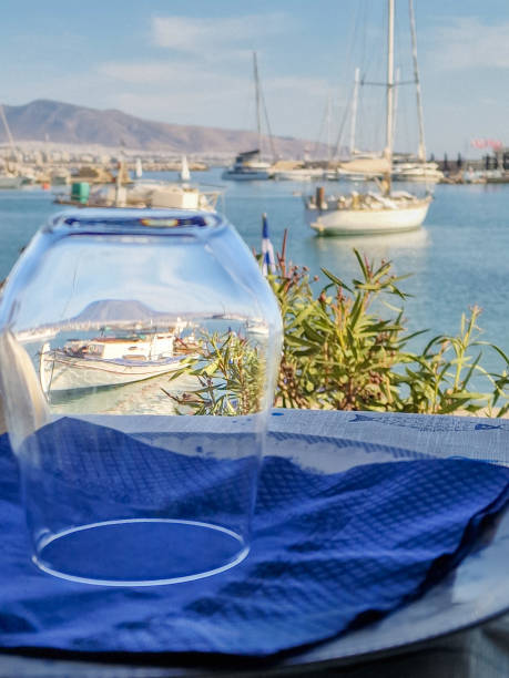 Fishing boat visible through a drinking glass inverted over a plate with other boats visible in the background in Mikrolimano harbour in Pireaus, Greece