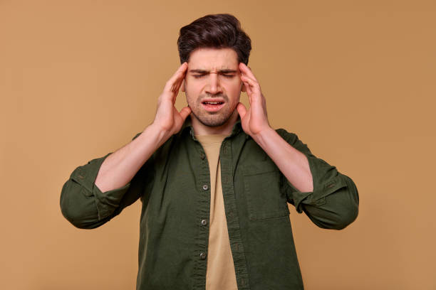 istock A Stressed Young Man is Holding His Head with Frustration Against a Brown Background 2197203626
