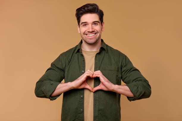 istock A cheerful man smiles and forms a heart shape with his hands against a warm, inviting background 2197203627