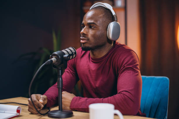 istock Male podcaster wearing headphones, speaking into mic while recording in home studio setting 2197212864