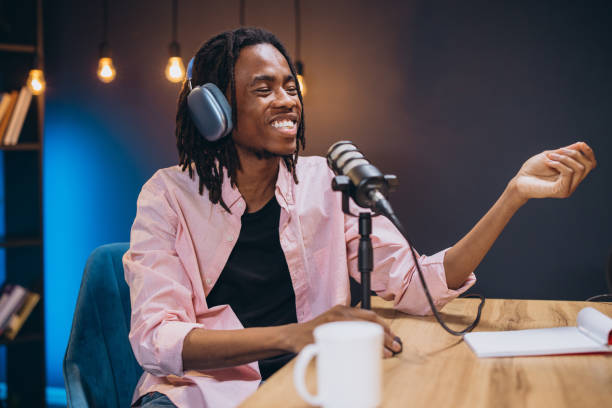 istock Dreadlocked podcaster wearing headphones, speaking into microphone while recording audio content in home studio setting 2197212887