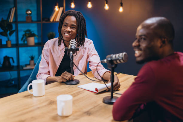 istock Two cheerful podcasters recording audio content in professional studio, using microphones and notepad 2197213004