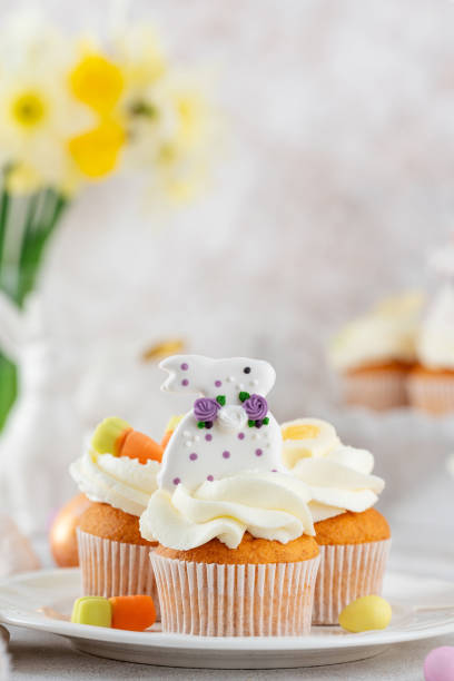 istock Easter cupcakes are decorated with cream, sugar bunnies, chocolate eggs, jelly carrots on a white plate. Easter food composition. Copy space. 2197213092