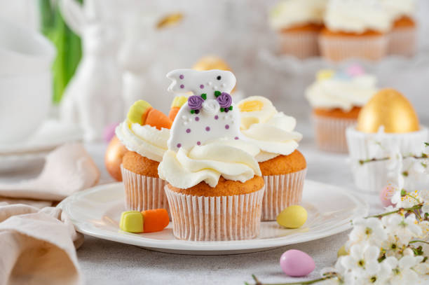 istock Easter cupcakes are decorated with cream, sugar bunnies, chocolate eggs, jelly carrots on a white plate. Easter food composition. Copy space. 2197213095