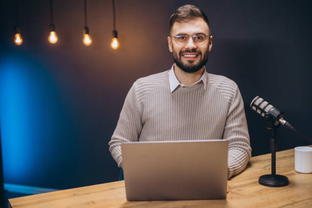 istock Young podcaster using a laptop and a microphone while recording audio content in a professional studio 2197215866