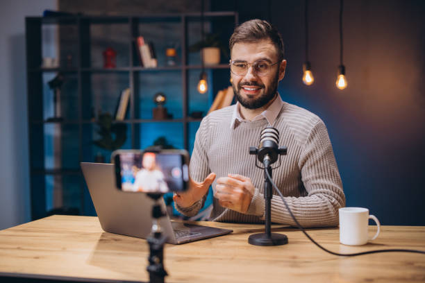 istock Male podcaster speaking into mic, recording digital content with smartphone in home workspace, wearing casual attire 2197215931