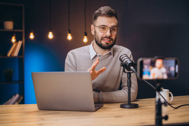 istock Young man recording a podcast using a professional microphone and laptop, talking and gesturing while looking at the camera 2197215934