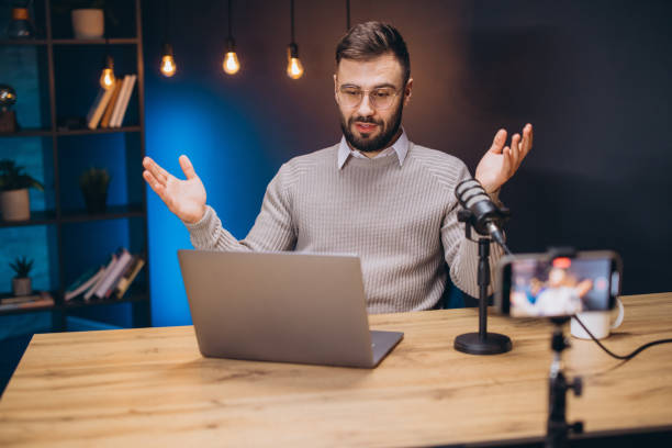 istock Podcaster working at home studio, speaking into microphone, laptop and smartphone nearby, using hands while talking 2197215939