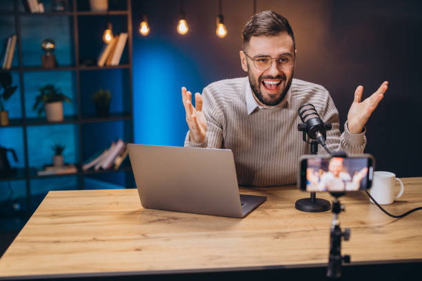 istock Happy male influencer gesturing while recording a podcast in his home studio using professional microphone, laptop and smartphone 2197216010