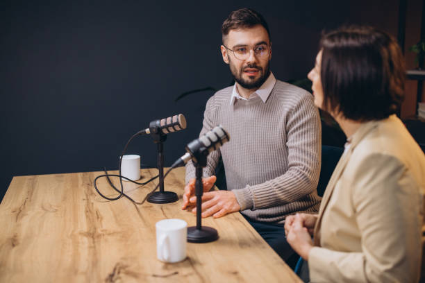 istock Podcasters discussing topics animatedly, sitting at sleek microphones inside contemporary recording studio with sound absorbing walls 2197216096