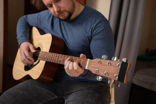 istock Man Practicing Acoustic Guitar at Home, musician sitting with instrument, learning to play chords 2197228918