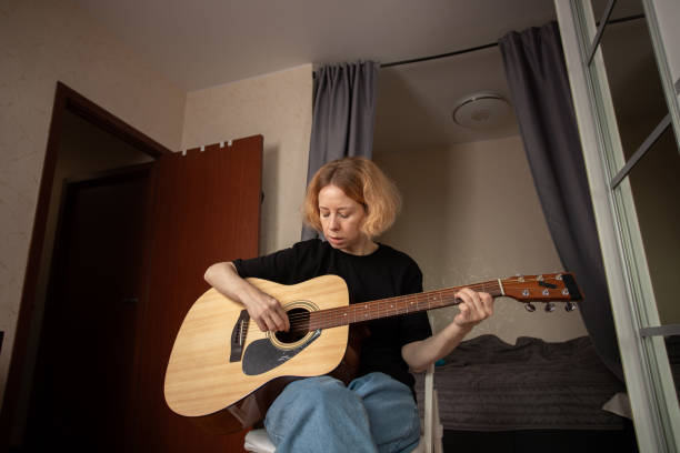 istock Woman Practicing Guitar in Cozy Bedroom, guitarist strumming strings, musical performance and learning experience. 2197229010
