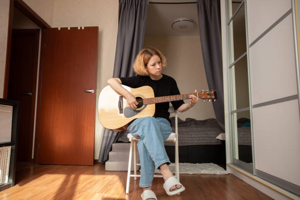 istock Woman playing acoustic guitar at home, hobbyist practicing guitar techniques, indoor focus on learning chords and wooden instrument sounds. 2197229016