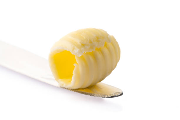Close-up of a knife spreading fresh butter with soft curls forming on the blade. Warm natural light highlights the creamy texture, creating a rustic and appetizing food scene.