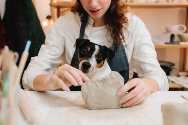 istock Potter with dog is making ceramic clay product on the table in the pottery workshop. Potter is sculpting wet clay for ceramics products. 2197232299