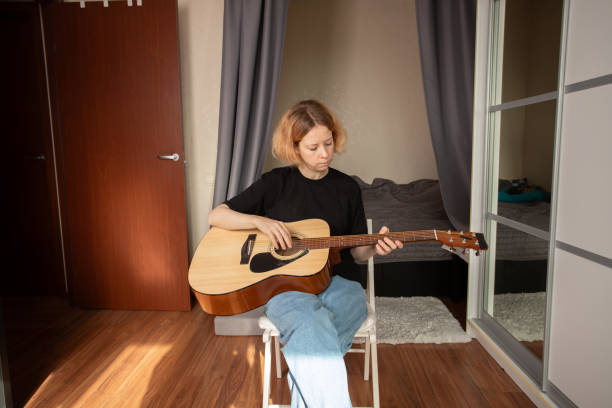 istock Woman Practicing Acoustic Guitar in Cozy Bedroom, learning to play with concentration, indoor hobby and skill development with acoustic guitar. 2197233090