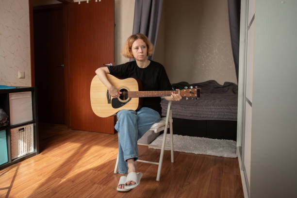 istock Woman playing guitar, engaging in music as a hobby, focused on learning and practicing chords. 2197233094