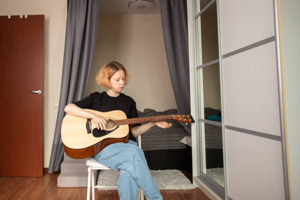 istock music lessons, Woman learning guitar, playful approach to learning, exploring country and rock styles, focusing on finger placement 2197233111