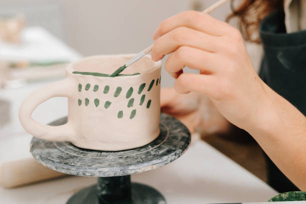 istock Artist is decorating and painting handmade ceramic clay cup in the creative workshop. Painter is drawing and adding unique designs to the earthenware. 2197233416
