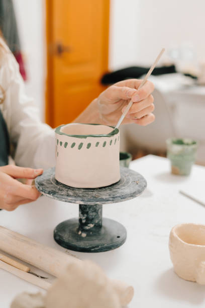 istock Artist is decorating and painting handmade ceramic clay cup in the creative workshop. Painter is drawing and adding unique designs to the earthenware. 2197233431