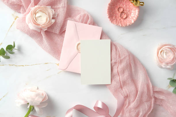 istock Wedding invitation card mockup, pink envelope, and delicate ranunculus flowers on a marble background. Flat lay, top view, copy space. 2197233461
