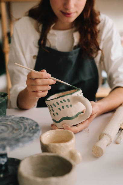 istock Potter draws an abstract design into earthenware cup. Experienced artist painting designs on ceramic cup in pottery workshop. 2197233538