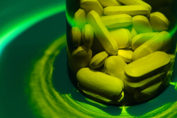 Yellow pills inside a glass container under green light, creating a vibrant and intriguing visual