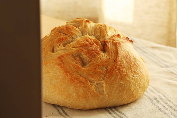 Homemade sourdough bread with a crispy, textured crust, resting on a striped cotton cloth, rustic and artisanal, warm natural tones, copy space