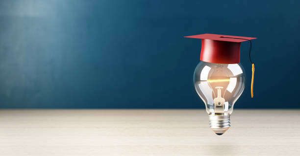 istock Lightbulb wearing a red graduation cap on wooden table, dark blue background. 3D Rendering 2197241181